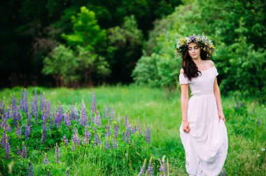 Güzellik kız açık havada zevk doğa. Kır çiçekleri başında bir çelenk kızla yol boyunca yürür.