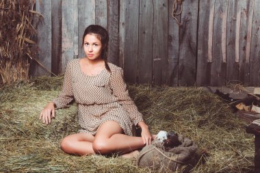 Saman üzerinde ayakları yalan ve kameraya bakarak bir torbayla oturan genç kız