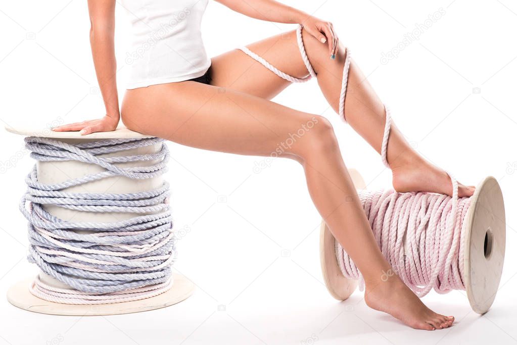 Slender woman's legs tied with rough rope. Elegant slender female legs, two rope bobbins.