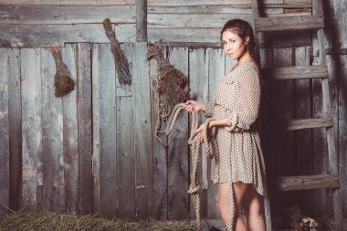 Dalgalı bir ahırda ip onun elinde tutan genç kız duvar süpürgeler ve merdiven arka ile. Kameraya bakarak