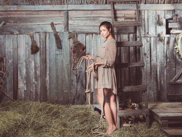 Genç kızla bir ip onun elinde, saman üzerinde ayakta tam uzunlukta bir ahırda arka duvarda dalgalı. Kameraya bakarak