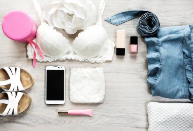 Moda kavramı. Moda kadın natürmort. Üstten görünüm için kadın kadın moda aksesuar. Kadın aksesuarları: beyaz dantel iç çamaşırı, cüzdan, cep telefonu, kot pantolon, tırnak cilası, dudak parlatıcısı, beyaz sandaletler
