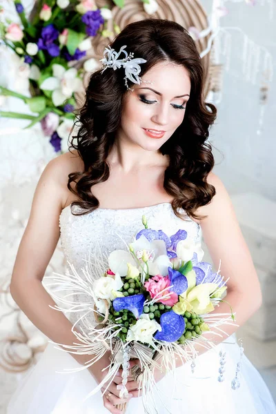 Lovely shy girl in a wedding dress and a curly hairstyle looking at a bouquet in her hands. Looking lowered down