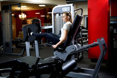 Çekici kız çalışma bizim büyük eğitim simülatör bir spor salonunda. Bacaklar vasıl jimnastik salonu için ağırlıklar basın makine kullanan sportif kadın. Güzel esmer simülatörde egzersiz. Onun dörtlü makinede çalışan.