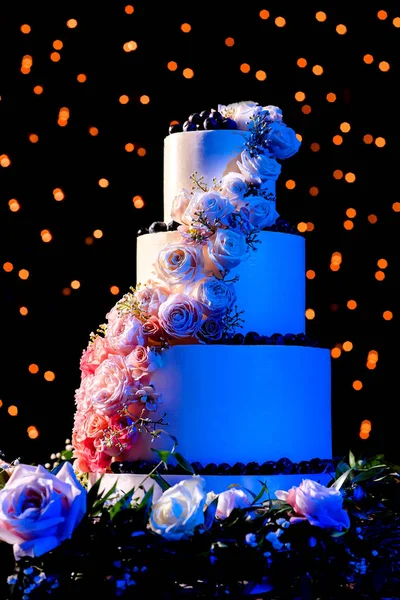 Picture of a beautiful wedding cake with roses and blue lighting with bokeh background