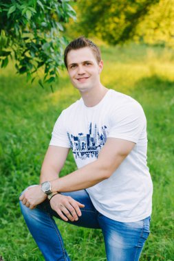 Parkta genç bir adam portresi. Bu kameraya gülümseyen, elleriyle dizlerinin üzerine eğilerek bir genç adamın geçti