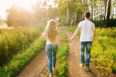 Genç çift, mutlu bir şekilde basılı tutup sallayarak orman yolu tarafından yürüyüş eller, sırtlarına kameraya