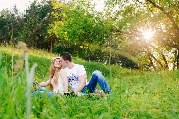 一对年轻的夫妇坐在一起在草地上 他亲吻她的脸颊 她的眼睛紧闭 — 图库照片