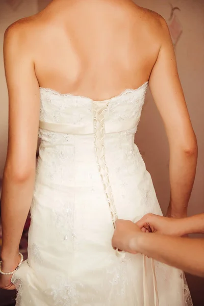 Wedding preparation. Female hands fastening buttons on a wedding dress, the bride is standing back to the camera