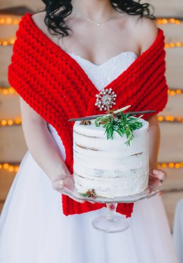 Genç gelin güzel bir pasta bir şeffaf cam stand üzerine beyaz holding ile kırmızı bir fular zıt elbise, düğün kış