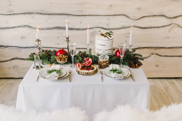 Composition of a new year dinner for a couple - an unusual cake, candles, tall glasses and fir branches, wooden background