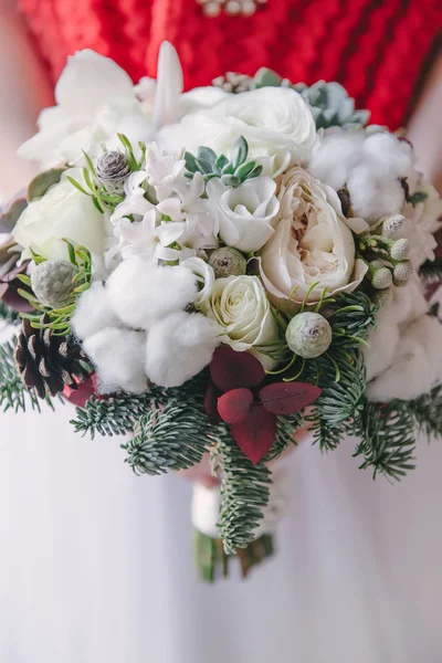 Close look on a bridal bouquet of white blowers and green branches, red cloth on the back. Christmas bridal bouquet