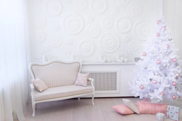Clean white room with original light christmas decorations in white and light pink shades. Interior living room with a Christmas tree and decorations.