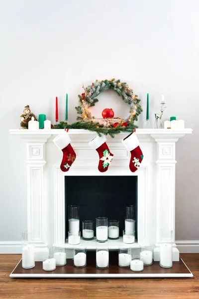伟大的白色壁炉装饰着许多蜡烛 绿松花圈和明亮的红色圣诞袜 — 图库照片