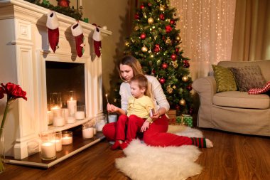 Şirin anne ve oğlu bir tüylü beyaz halı ışık mumlar birlikte bir çift gördüm. Genç Anne ve oğlu bir şömine Noel tarafından
