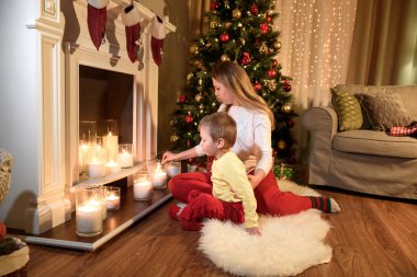 Mum onun küçük oğlu, yeni yıl zaman, parlak ışıklar ile düz genç anne. Genç Anne ve oğlu bir şömine Noel tarafından