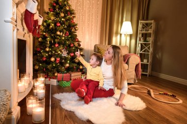 Güzel anne dikkatle ne oğlu ona, Noel günü onun parmak işaret çorap söylüyor için dinleme tatil kış bir şömine üzerinde asılı. Anne ve oğlu bir karanlık oturma odasında şömine başına oturmuş