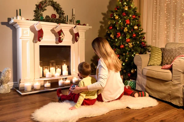 若いママと近くの蝋燭が付いている暖炉 空気中にクリスマス魔法一緒に座っている少年の画像をバックアップします 母と息子のクリスマスに暖炉のそばで 冬とクリスマスの休日の概念 — ストック写真