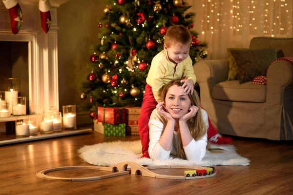 Sevimli küçük oğlan yalancı annesinin geri tırmanma, yeni yıl geleneksel olarak oda dekore edilmiştir. Mutlu Noeller ve mutlu yeni yıl. Güzel genç anne ile oğlu