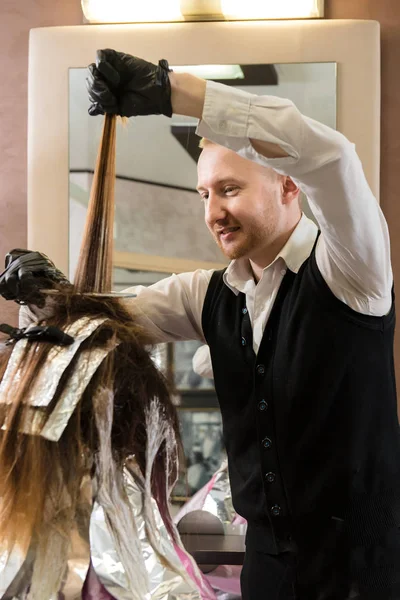 Stylist with hair dye and brush coloring hair at salon. A picture of a cool hairdresser brushing his client\'s hair in a specific way