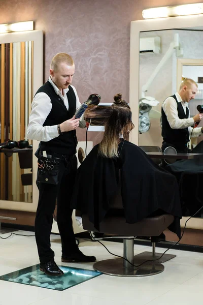 Hairdresser doing haircut for woman in hairdressing salon. Concept of fashion and beauty. A professional hairdresser in work, drying a client\'s hair, comfortable room with a huge mirror