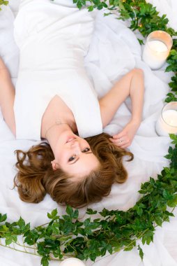 Fotoğrafta baş aşağı uzanmış güzel bir genç bayan saçlarına hafifçe dokunuyor kameraya dostça bakıyor ve büyüleyici bir şekilde gülümsüyor. Güzel fotoğraf, güzel saç..