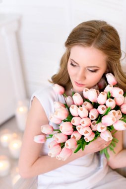 Genç, utangaç ve nazik bir bayanın portresi. Boynuna bir sürü pembe lale dokunuyor. Bahar kadınlarının moda tarzı fotoğrafı. Çiçekli güzel bahar kadını