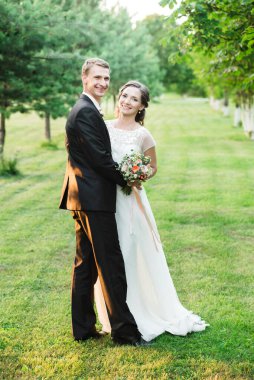 Mutlu çift, yeşil bir bahçede birbirlerine sarılırken mutlu bir şekilde gülüyor.