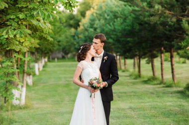 Bir yaz bahçesinde gelininin alnını öpen takım elbiseli genç damat. Romantik Evli Genç Aile