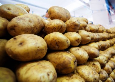 Sokak pazarında satılık patatesler. Tezgahın üzerinde büyük patates kütükleri var.