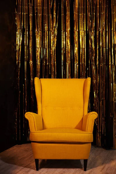 Yellow armchair on a background of a black gold wall.