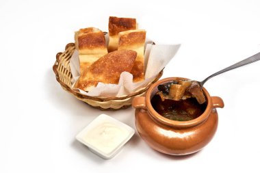 Bir dilim ekmek ve ekşi kremayla servis edilen bir çömlek mantar çorbası. Bir kafede, restoranda menü için yemek servisi yapıyorum. Beyaz arkaplanda izole