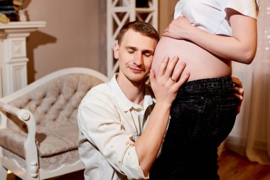 Karını kucağında tutan genç koca karnının içindeki bebeği dinle ve duy. Koca oturur ve karısına sarılır. Hamile ve yeni doğan çocuk kavramının sevgisi ve bakımı.