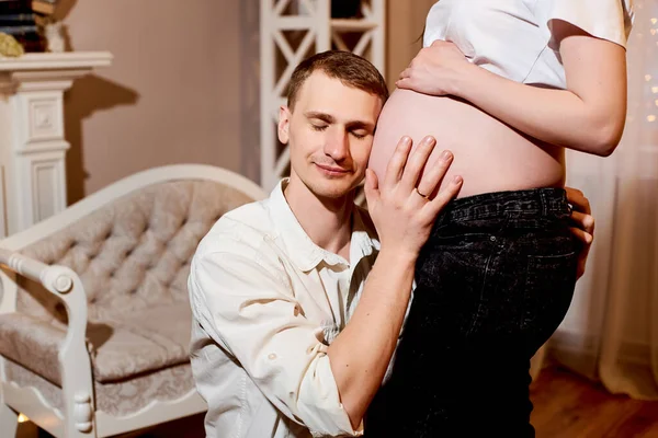 年轻的丈夫抱着妻子肚子 听着妈妈肚子里的婴儿 丈夫坐着拥抱妻子 爱和照顾怀孕和新生儿的概念 — 图库照片