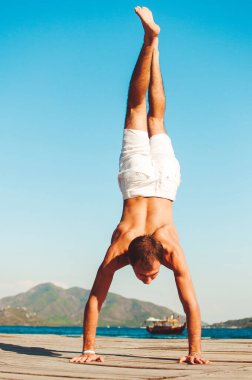 Güçlü, sağlıklı, yakışıklı atletik adam sabah egzersizlerini yapıyor. Mavi okyanus ve arkasında başka bir ada var..