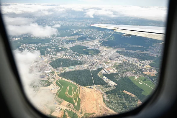 Abstract high angle air view of industrial landscape from airplane. Windows with light white clouds with window and airplane wing. Aerial photograph.