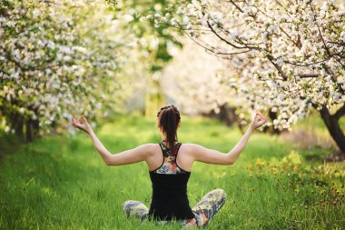 Yogi kızı yeşil çimlerde oturuyor, ellerini kaldırıyor Padmasana egzersizinde meditasyon yapıyor, dikiz aynasında.