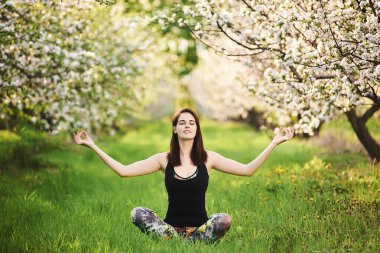 Yogi kızı yeşil çimenlerde oturmuş Padmasana egzersizinde meditasyon yaparken ellerini kaldırıyor. Uyum kavramı