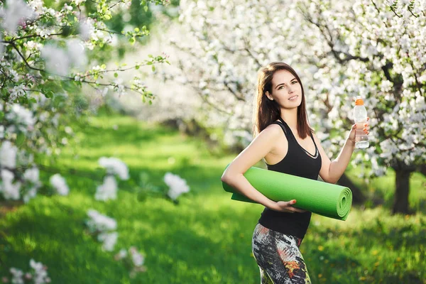 面带微笑的女人拿着水瓶和健身垫在花园里锻炼 积极的生活方式坦率的健身理念 — 图库照片