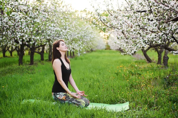 Young caucasian yogi woman with meditating seated during morning exersize on the green lawn in blooming garden, practicing breathing yoga in Virasana,outdoors meditation reduces physical fatigue