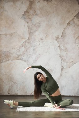 Çekici genç bir kadın evde esneme egzersizi yapıyor, yoga stüdyosunda çalışıyor. Yoga çalışıyorum, uzun süre kapalı alanda çalışıyorum. Eklemler ve bağlar için esneklik kavramı. Reklam alanı