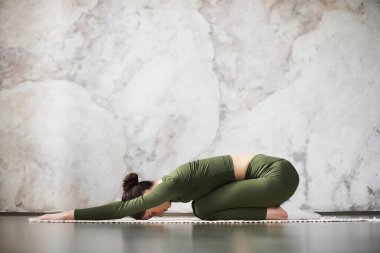 Güzel genç model kız evde çalışıyor, siyah ahşap zeminde yoga egzersizi yapıyor, çocuk pozu, Balasana Duruşu 'nda yatıyor, antrenmandan sonra dinleniyor, yandan bakıyor. Tam uzunluk, kenar görünüm