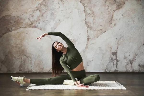 Sağlıklı genç bir kadın evde yoga yapıyor grunge duvar bej rengi arka plan, yoga minderinin üzerinde uzun boylu, esnek bir vücut, kapalı gözlerle rahatça gülümsüyor. Sağlıklı Yaşam Tarzı Konsepti.