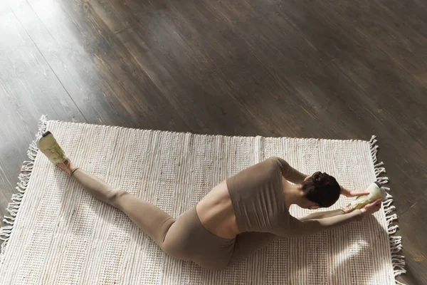 年轻的黑发女子做伸展运动躺在黑色的木制地板上 在家中或瑜伽工作室的天然地毯上 俯瞰全景 关节和韧带的弹性概念 复制空间 — 图库照片