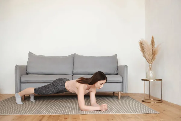 身材苗条的年轻女子一个人在客厅里做早操 靠着手肘站在木板上 在家锻炼为健康的身体 生活方式的概念 复制空间 侧视图 — 图库照片