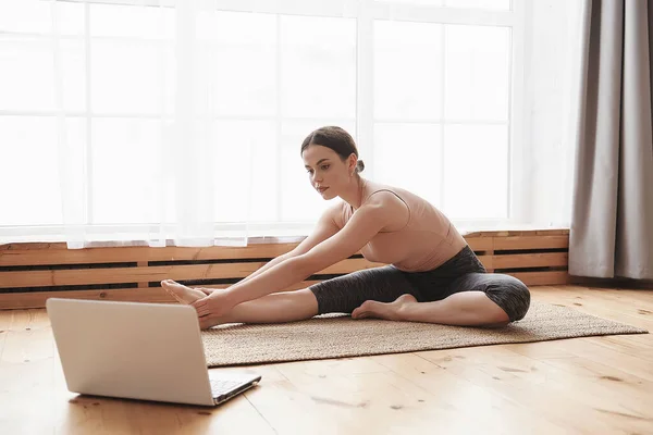 年轻女子练习瑜伽伸展 观看专业健身教练的网上视频辅导 在家锻炼 因为社交上的疏远 在线学习的概念 — 图库照片