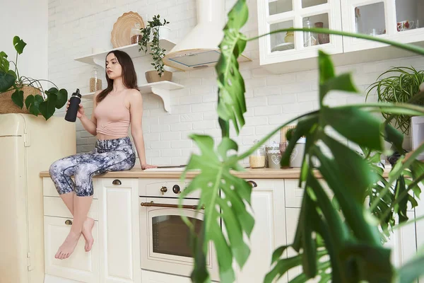 在家里厨房里一个穿着慢跑服的漂亮姑娘的画像 时尚运动服的概念 对成功和运动身体的渴望 看着相机 垂直的照片 健康的生活方式 — 图库照片