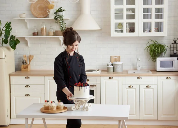 身穿黑色衣服的年轻女糖果工在厨房里干活 她把一个漂亮的浆果蛋糕和糕点放在桌上 生活方式烹饪的概念 复制空间 — 图库照片