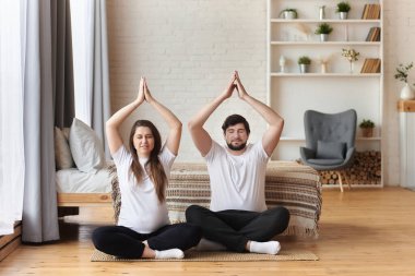 Genç bir çift güzel hamile kadın ve yakışıklı koca yoga ve egzersiz yapıyor, elleri Namaste 'de oturuyor ve evde kapalı gözlerle meditasyon yapıyor, hamilelik yogası, fitness konsepti.