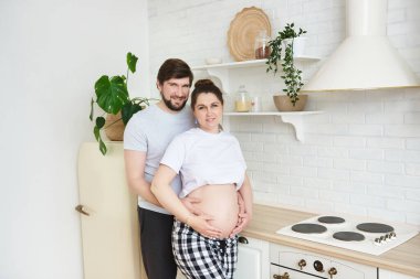 Müstakbel aile üyeleri mutfakta kameraya bakarak kucaklaşırlar. Sağlıklı yaşam tarzı, ebeveynlik, annelik, annelik, çocuk beklentisi. Aile hamileliği kavramı, kopyalama alanı.